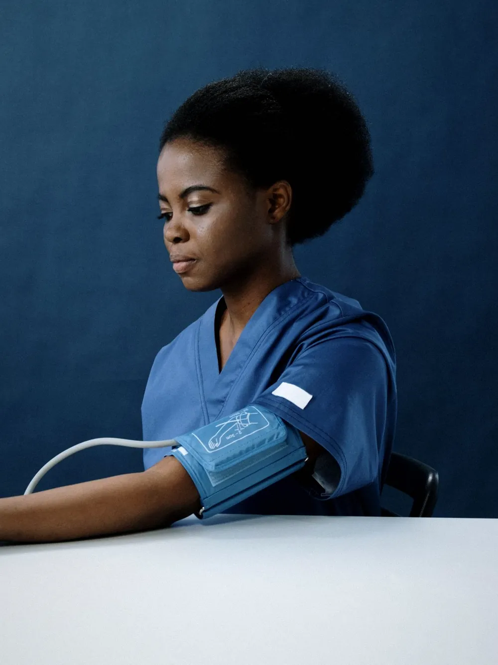 A nurse in blue scrubs taking a blood pressure reading