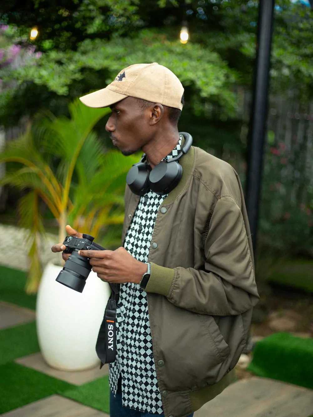 A photographer in a cap holding his camera in a garden
