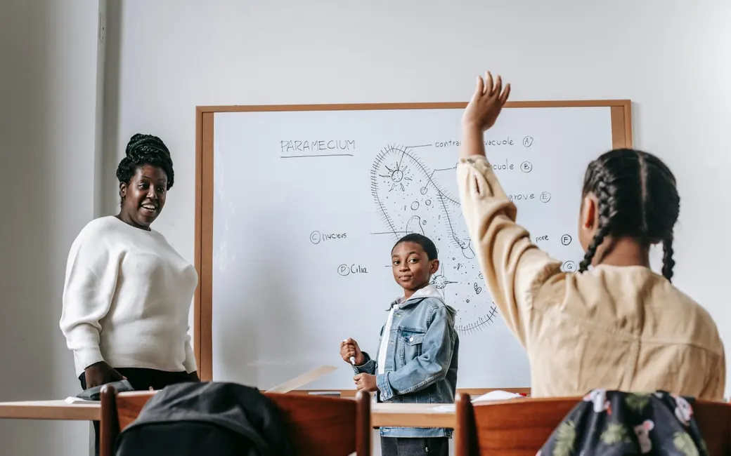 A teacher at the whiteboard while a pupil raises her hand